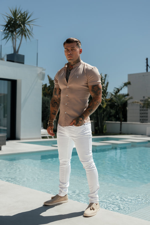 A person standing poolside wearing white trousers and a beige shirt.